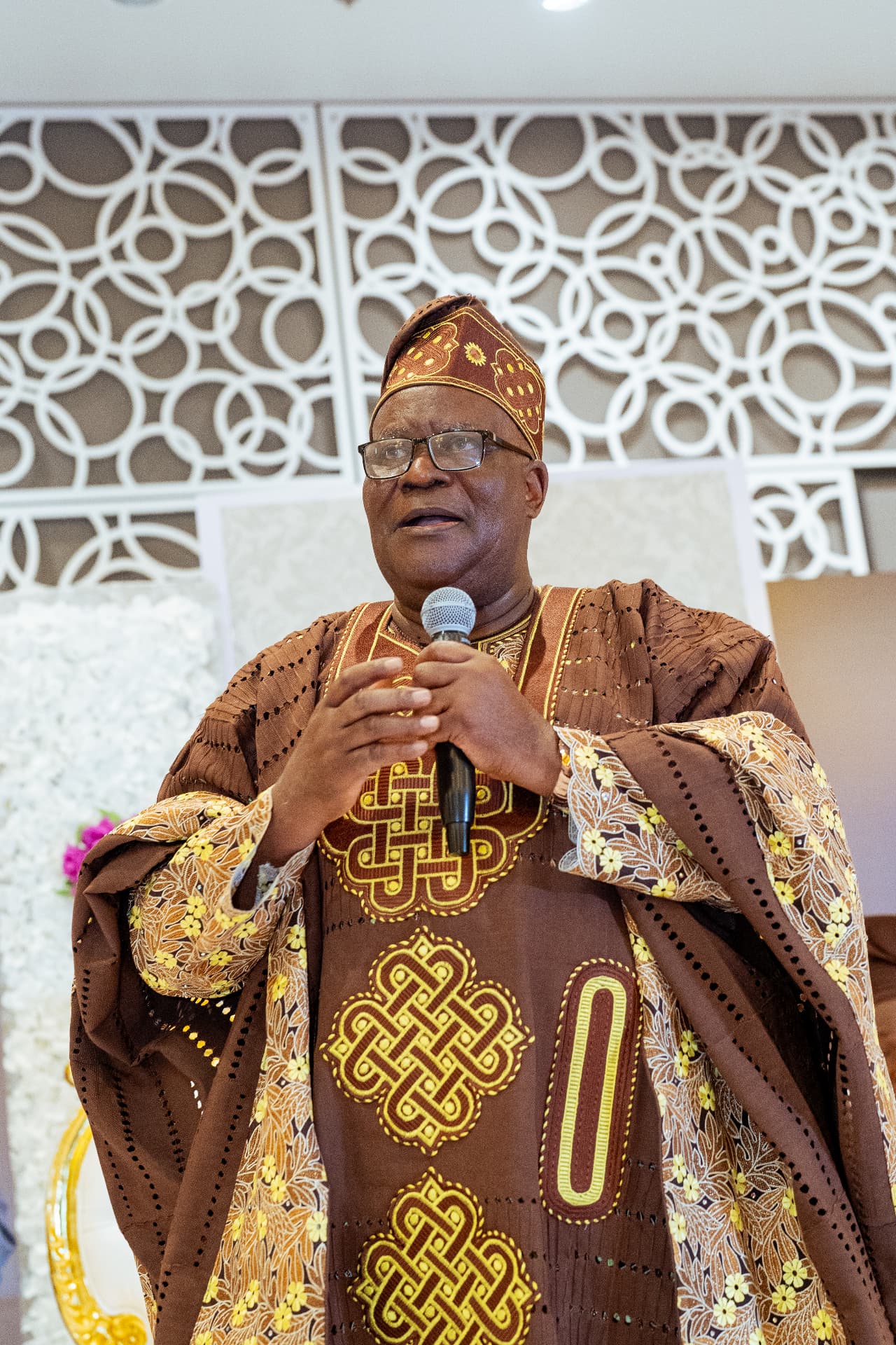 Apostle Odeneye speaking with a microphone in brown agbada